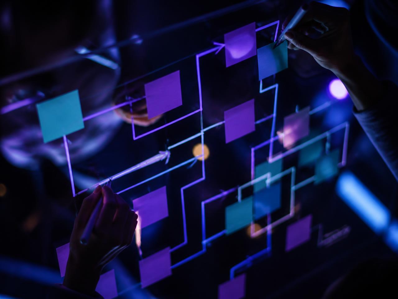 Hands mapping a connected customer journey on an illuminated glass board